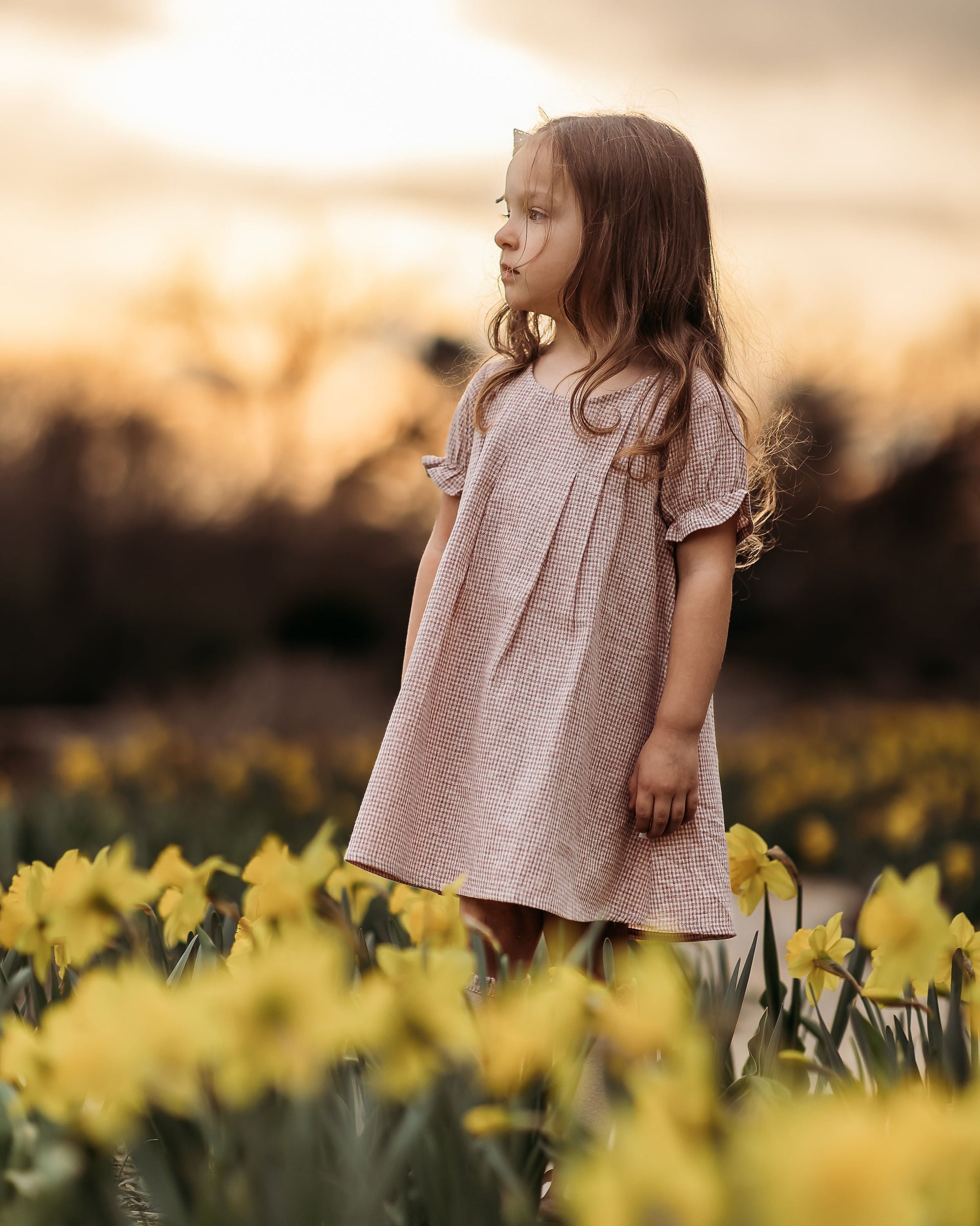 Young girl in a pink dress standing in a field of yellow flowers with a blurred background