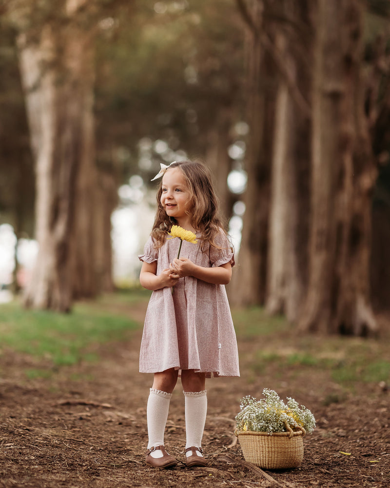 Young girl in a pink dress standing in a forest with a basket of flowers.