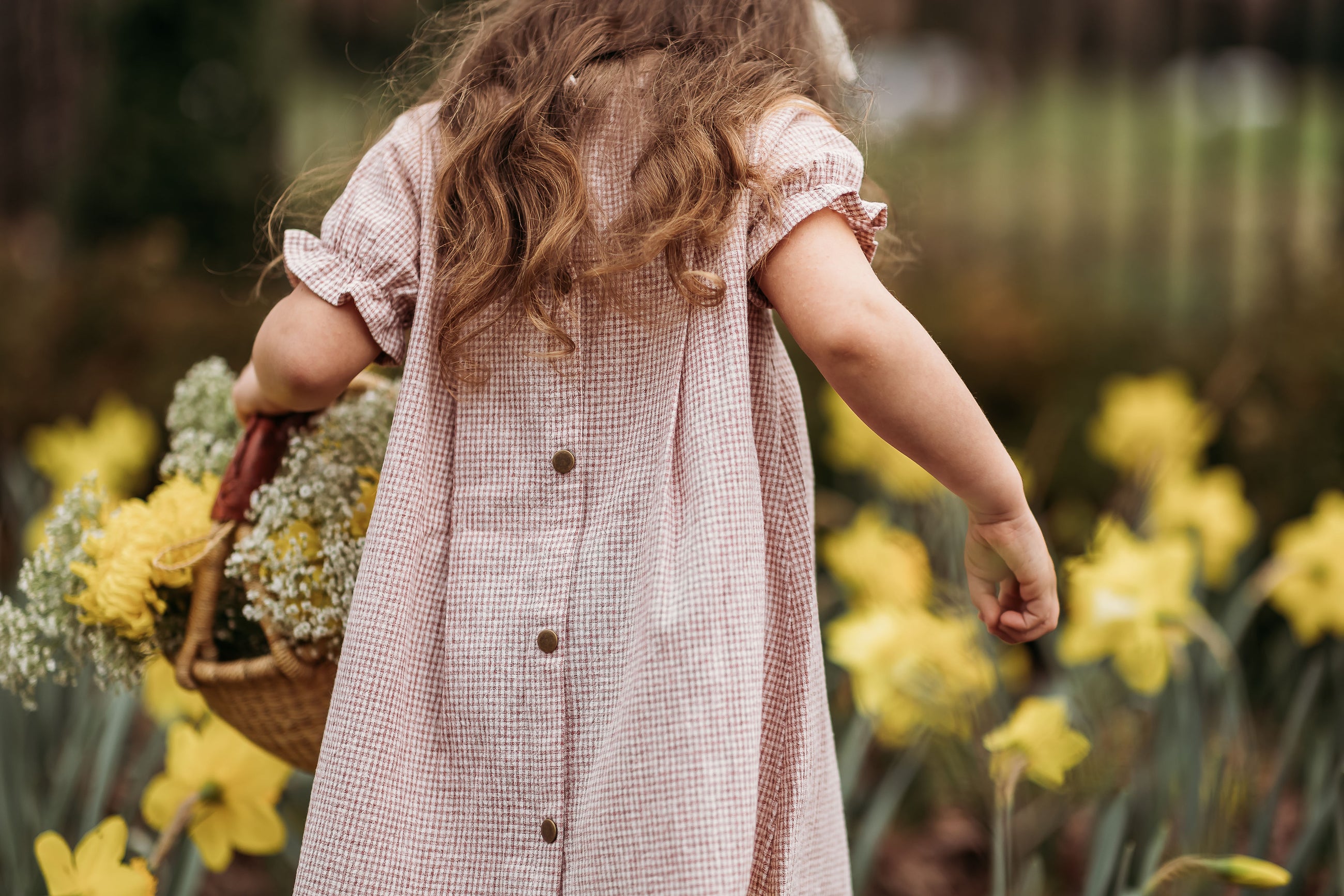 Child in a pink dress holding a basket of flowers in a garden with yellow flowers.