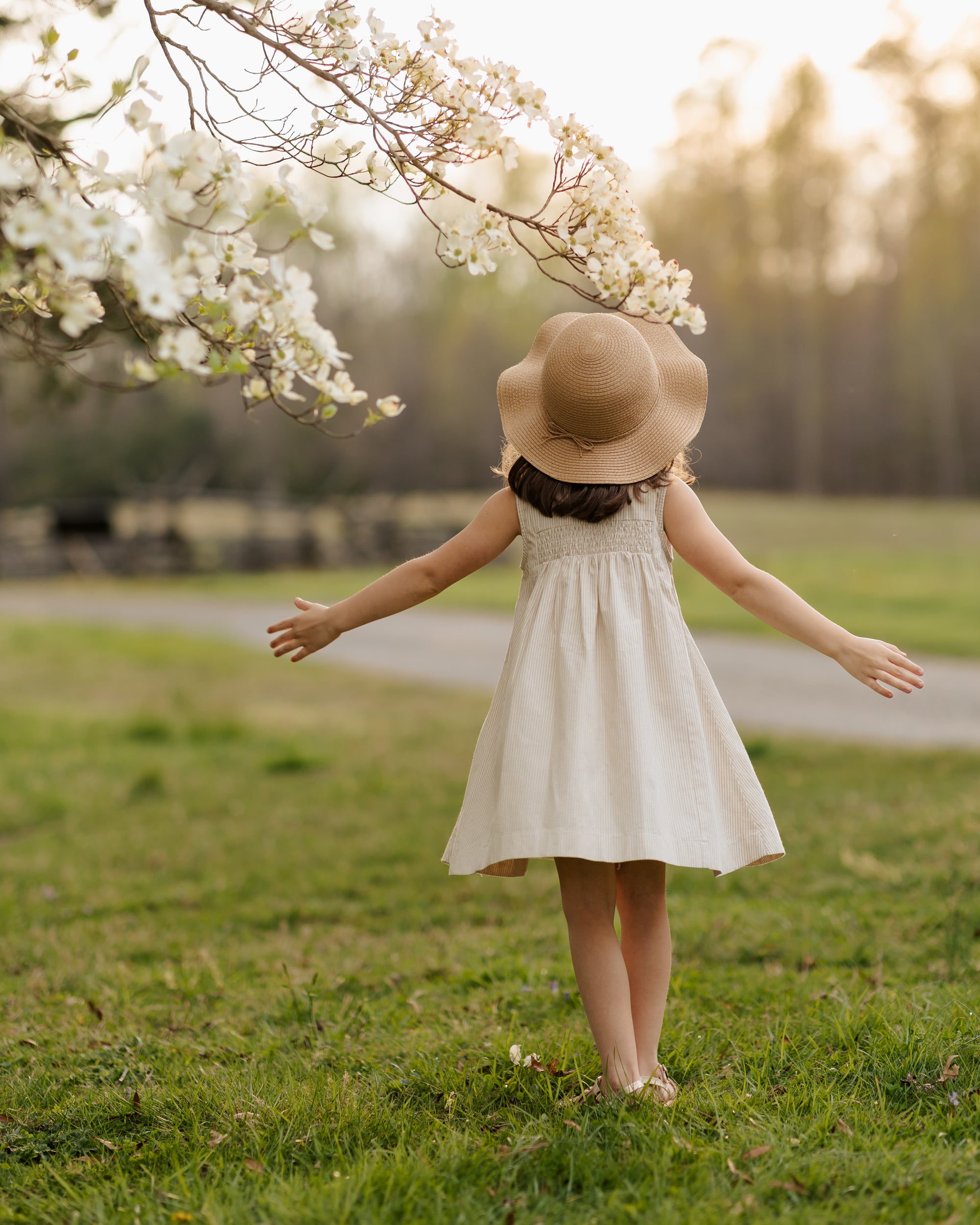 Petite 6-year-old model spinning in Beige Stripes Dress with white contrasting collar and button placket, showcasing the intricate back design, highlighting the adorable smocking and pleat accents, capturing the playful elegance of sustainable children's wear.