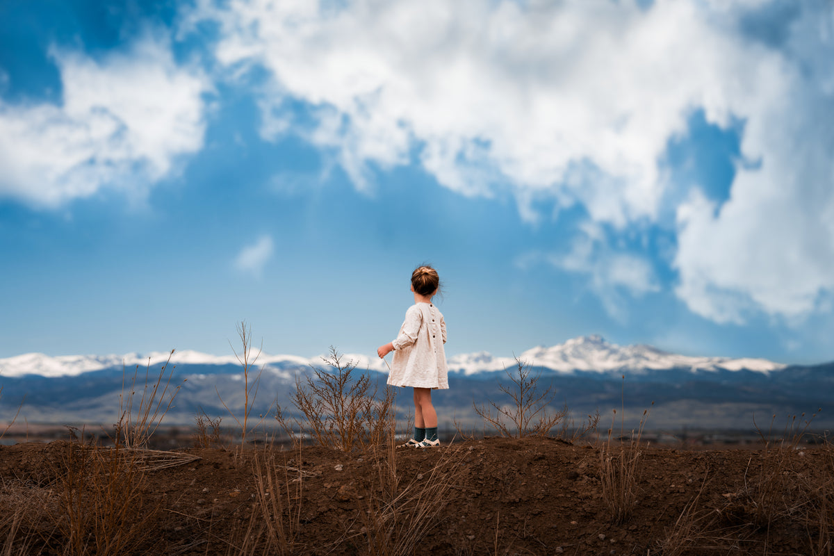 Girl standing in a field with mountains and blue sky in the background