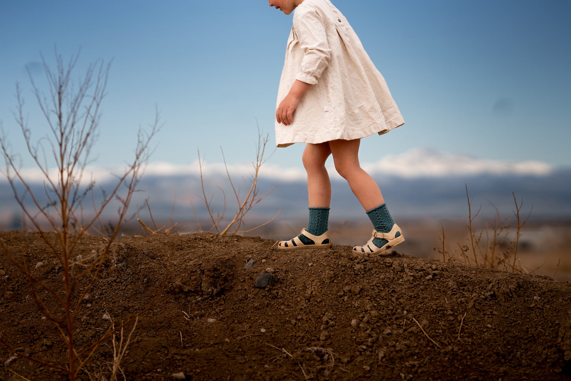 Person in a white dress standing on a dirt patch with a blurred landscape in the background