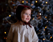 Child wearing a red bonnet in front of a decorated Christmas tree with lights.