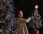 Child decorating a small Christmas tree with a star ornament against a dark background