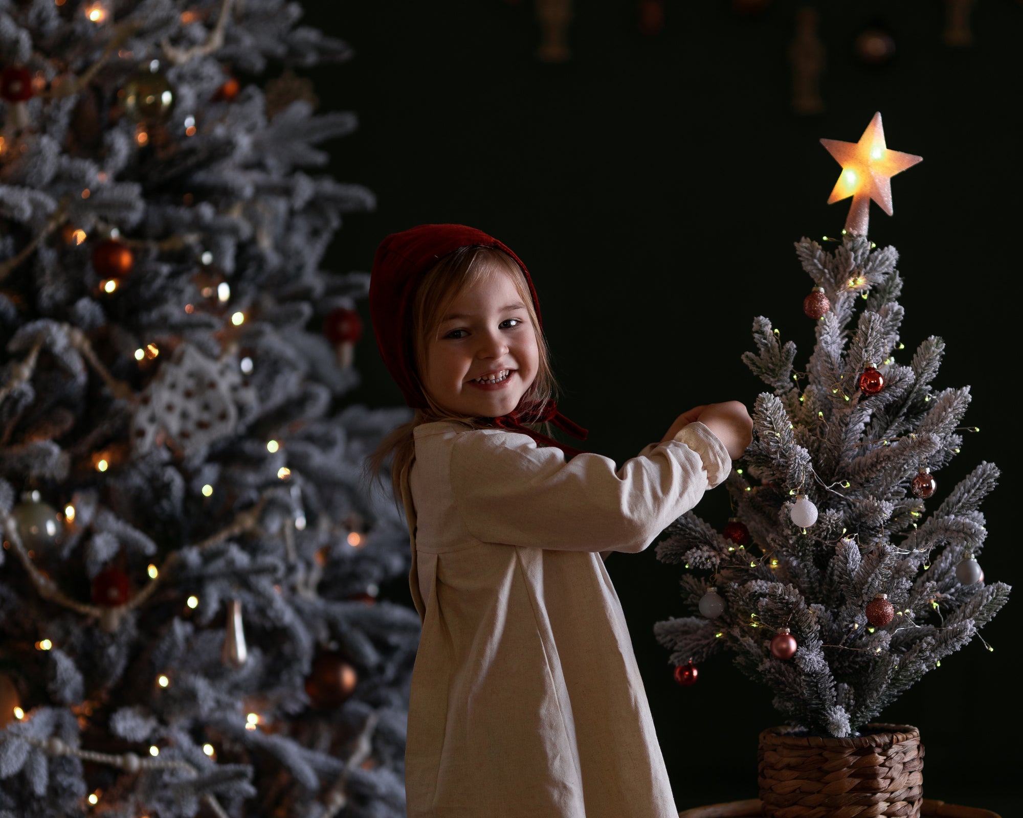 Child decorating a small Christmas tree with a star ornament against a dark background