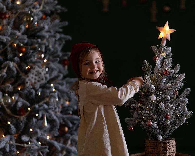 Child decorating a small Christmas tree with a star ornament against a dark background